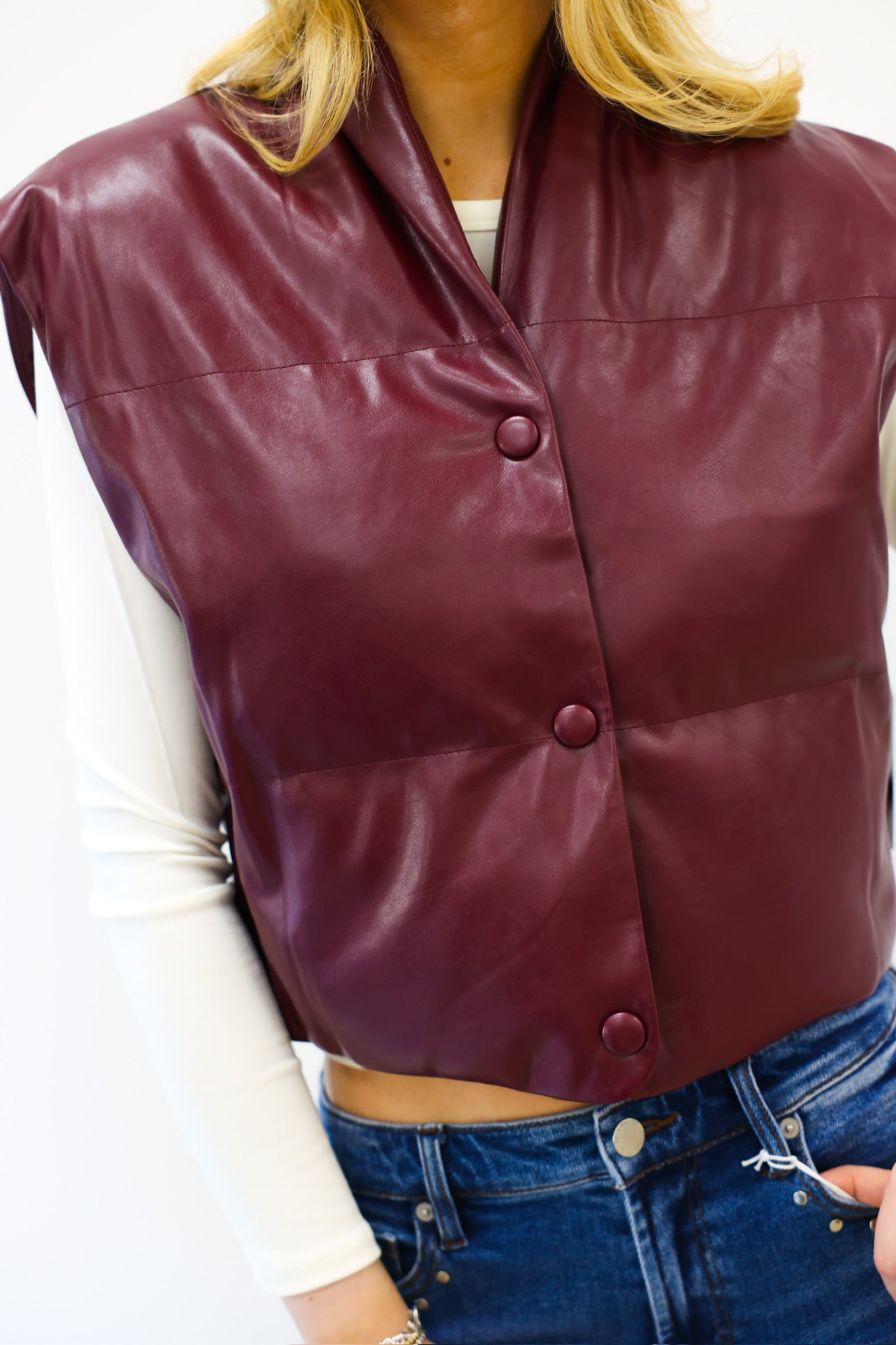 Maroon leather vest worn by a person with a white shirt and blue jeans.