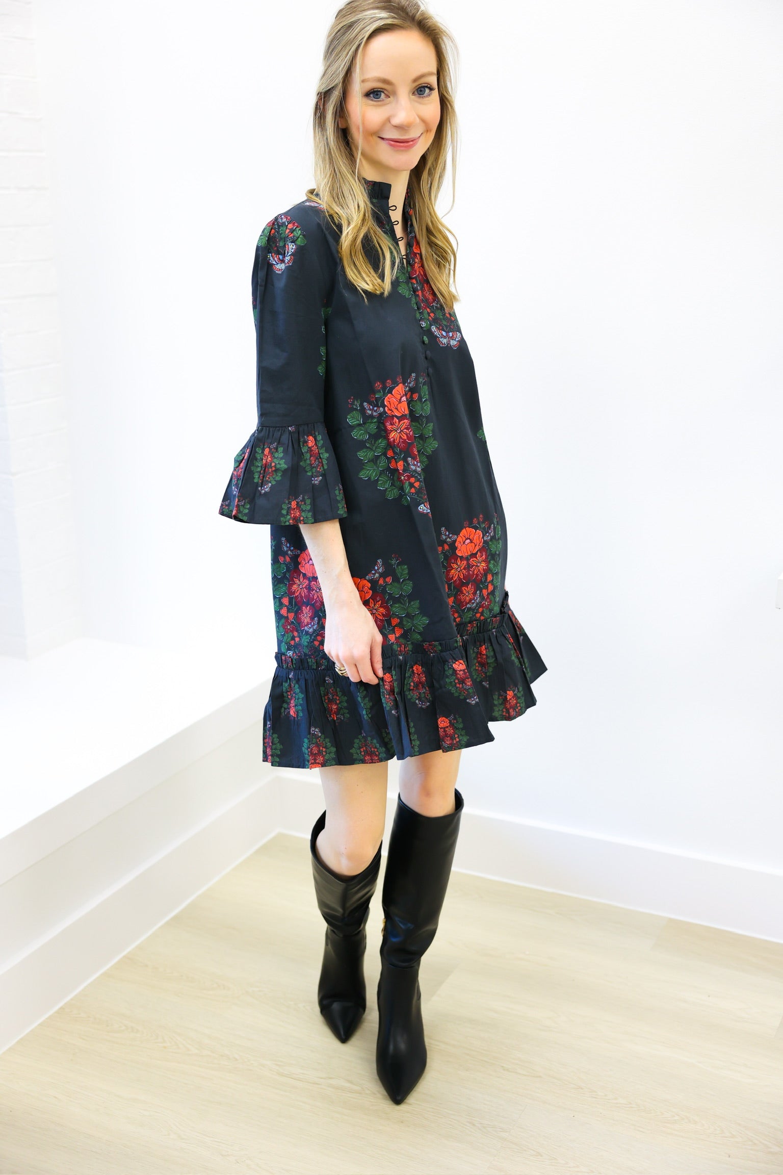 Woman wearing a dark floral dress with black boots on a white background