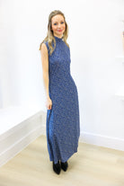 Woman wearing a blue patterned dress against a white wall.