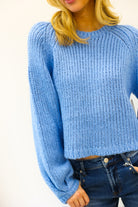 Person wearing a blue knitted sweater and jeans on a plain background