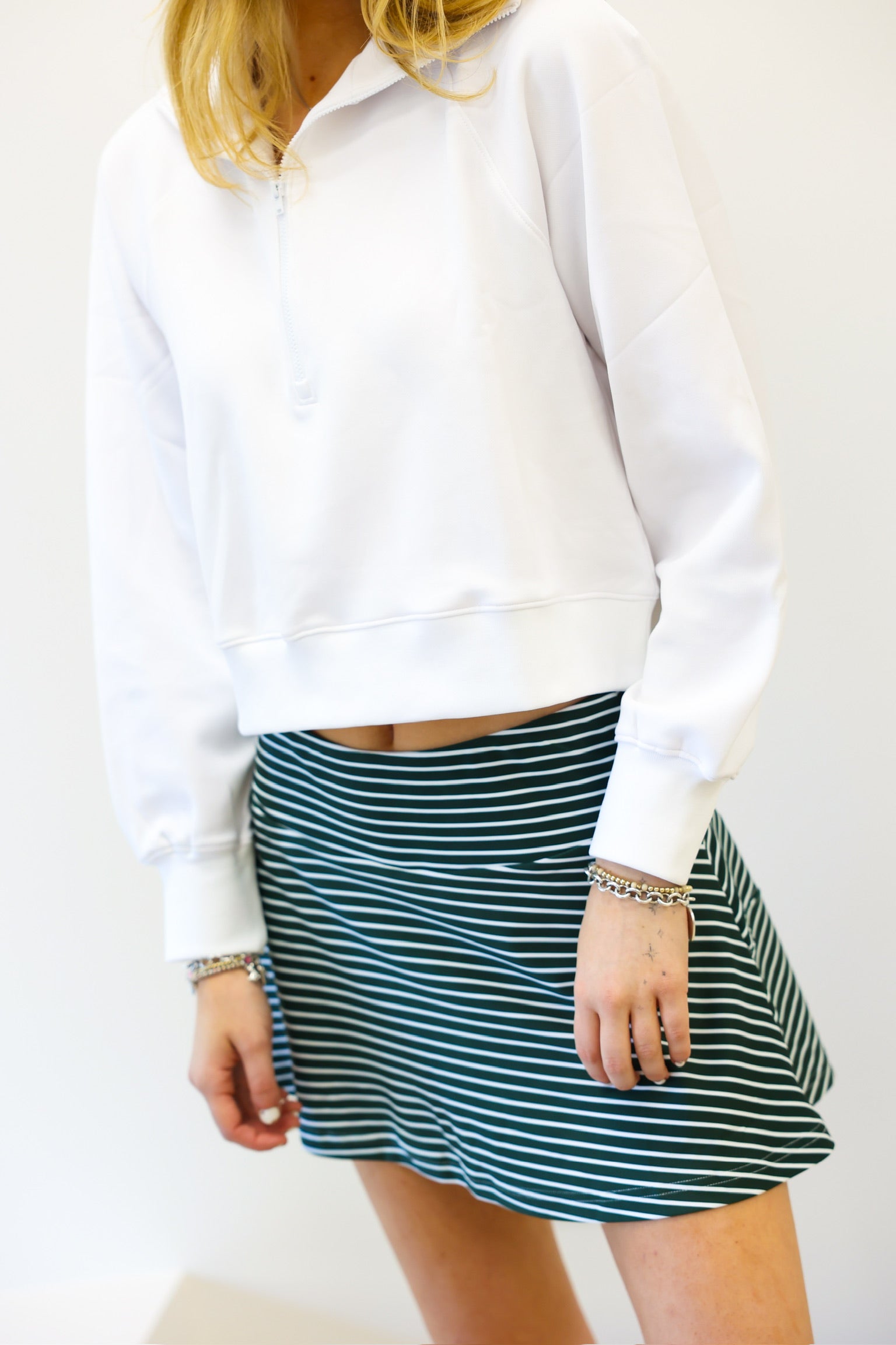 Person wearing a white sweater and green striped skirt on a plain background