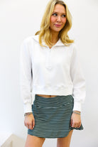 Woman wearing a white sweater and striped skirt against a plain background