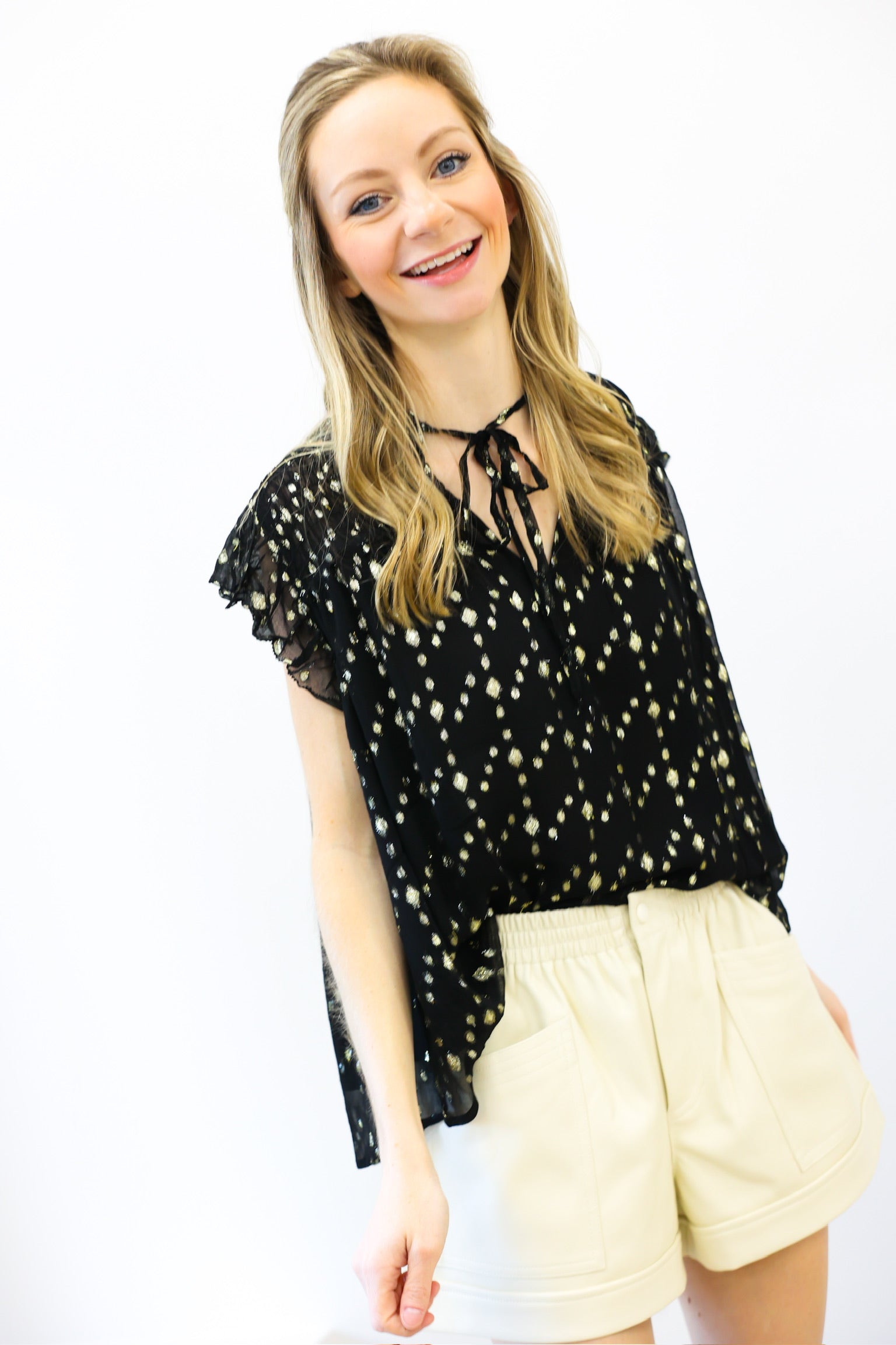 Woman wearing a black top with white patterns and beige shorts on a white background