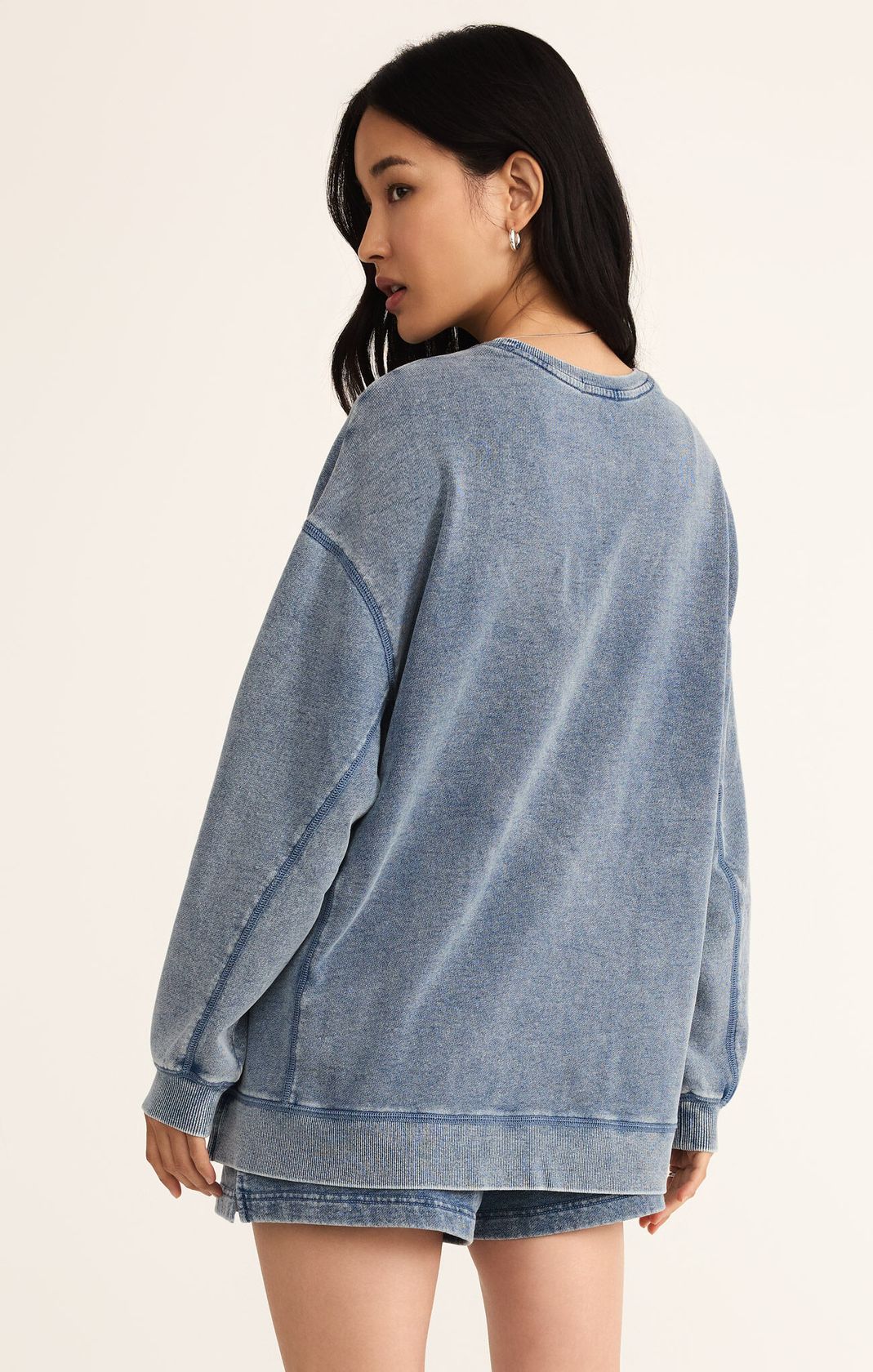 Woman wearing a blue sweatshirt and denim shorts on a beige background