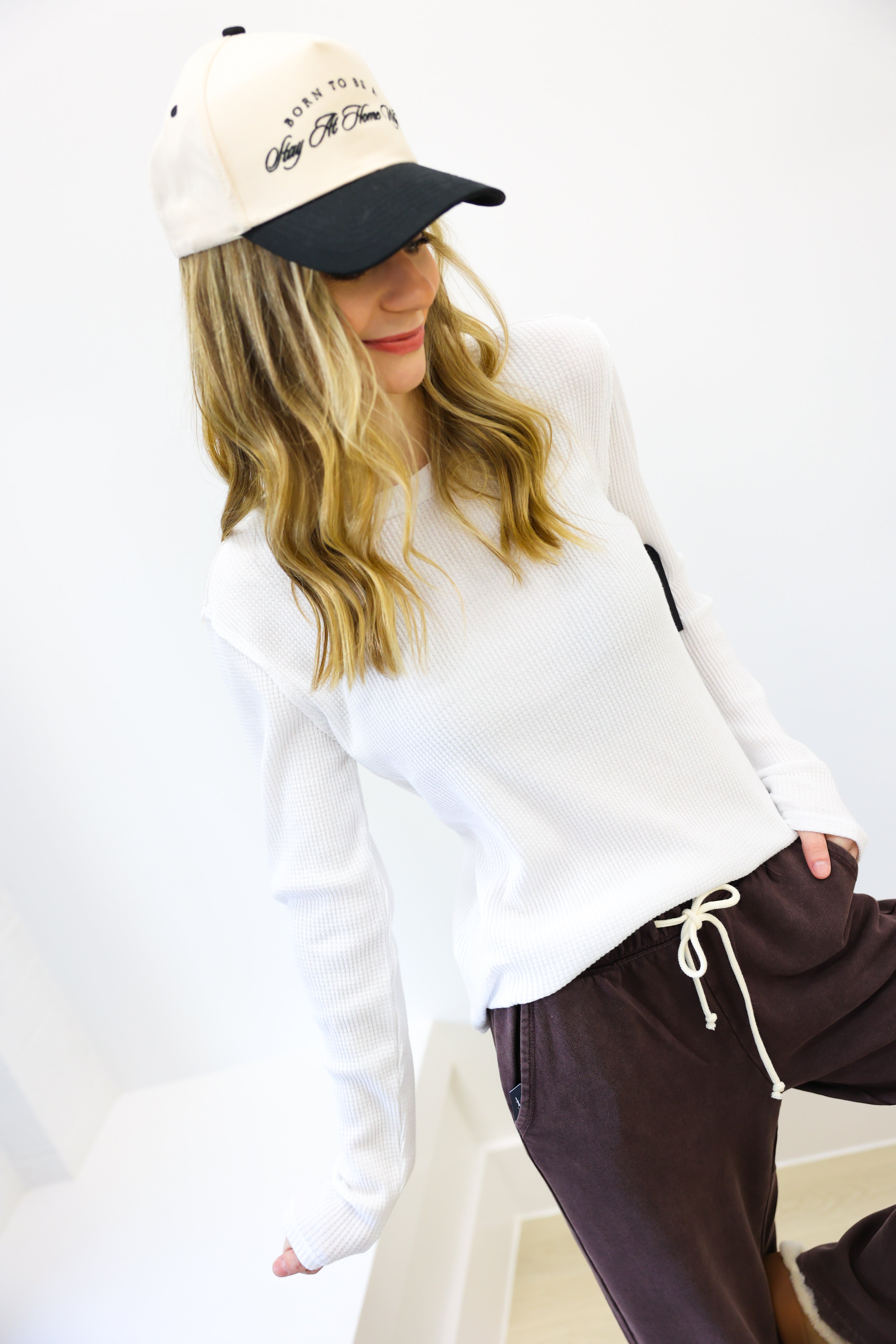Person wearing a white sweatshirt, brown pants, and a black and white cap on a white background