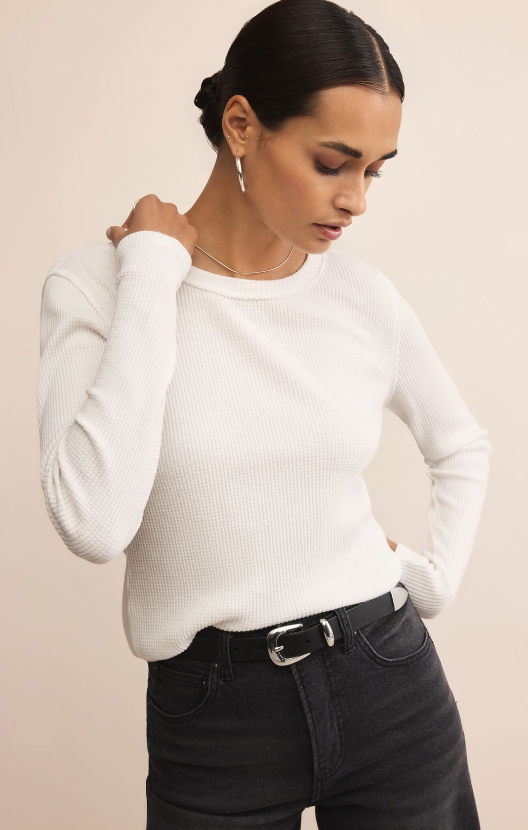 Woman wearing a white sweater and black pants against a beige background