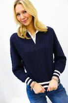 Woman wearing a navy sweater with white trim and blue jeans on a white background