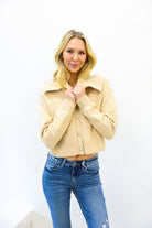 Woman wearing a beige cropped jacket and blue jeans against a white background