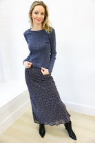 Woman wearing a blue sweater and patterned skirt against a white wall.