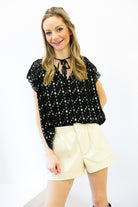 Woman wearing a black blouse with white polka dots and beige shorts on a white background