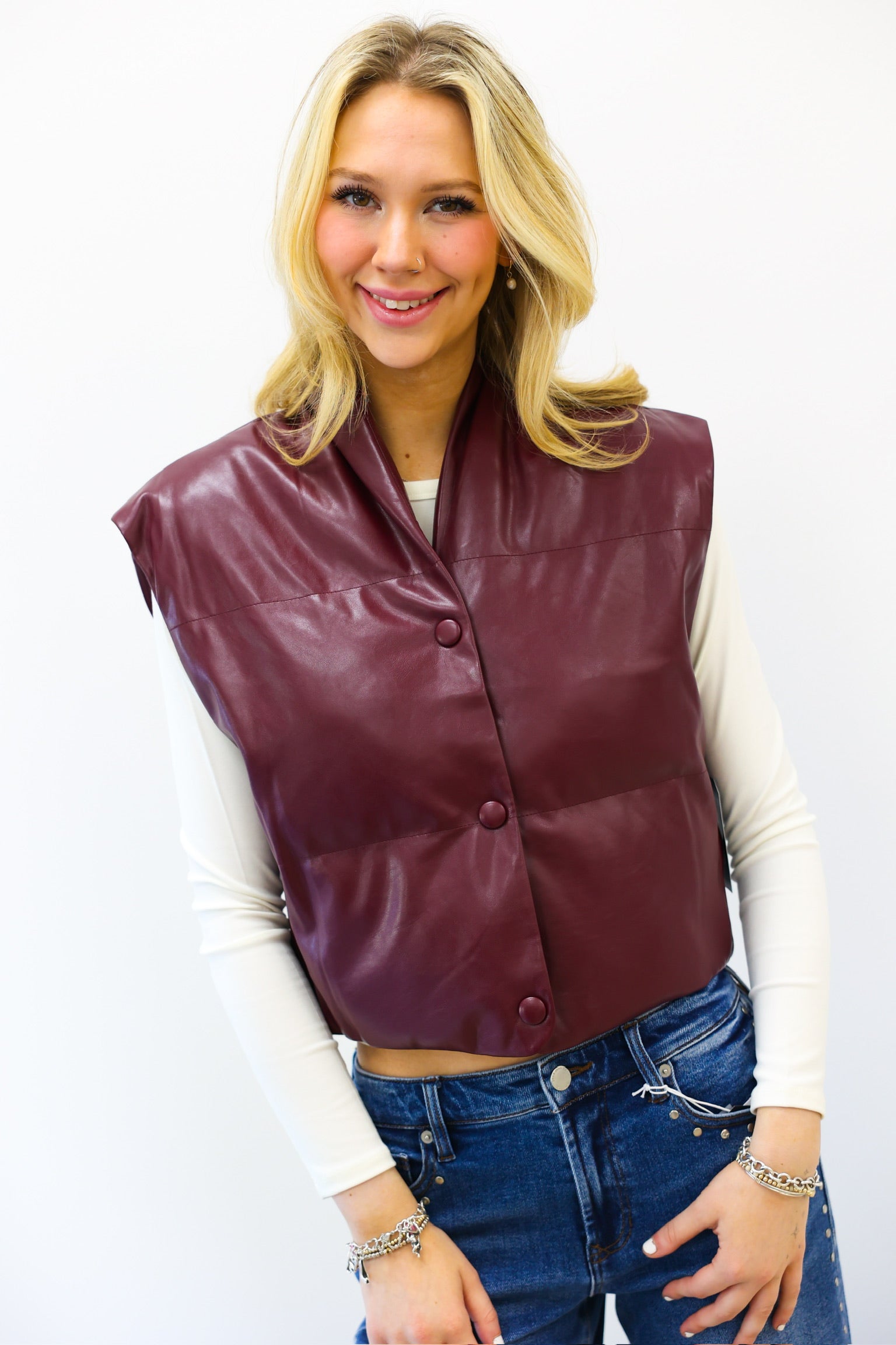 Woman wearing a maroon vest over a white long-sleeve shirt and blue jeans on a white background