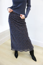 Person wearing a blue sweater and patterned skirt on a plain background