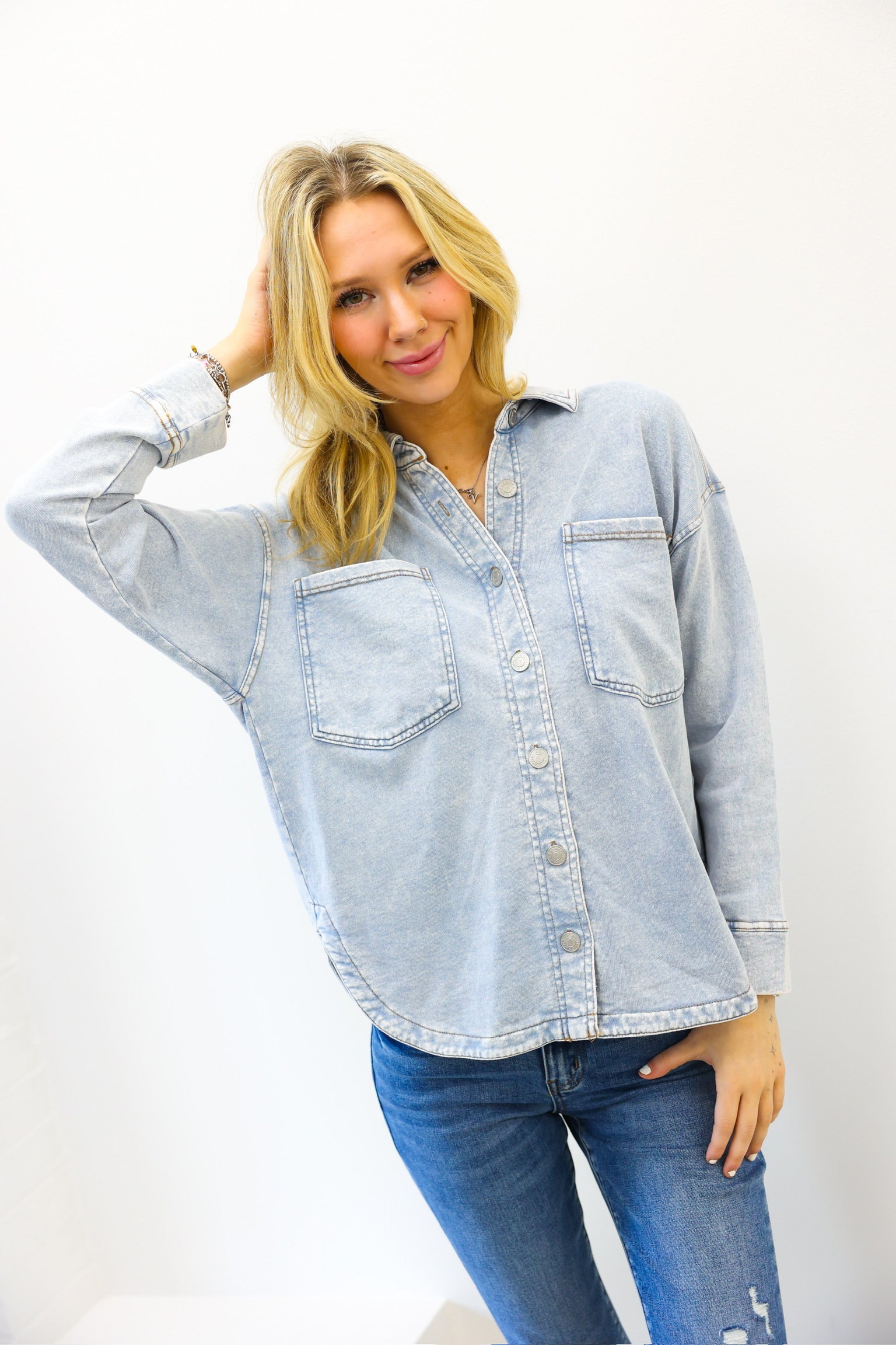 Woman wearing a light blue denim shirt and jeans against a white background