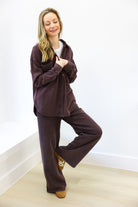Woman wearing a brown tracksuit posing against a white wall.