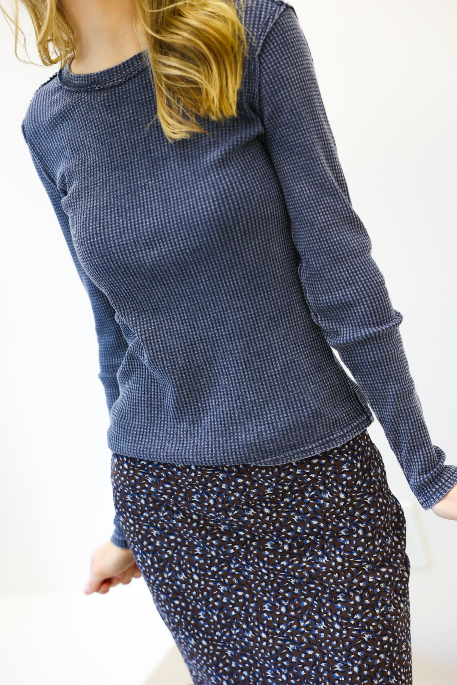 Person wearing a blue textured sweater and patterned skirt on a white background