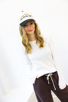 Woman wearing a white long-sleeve shirt and dark pants with a white cap on a white background