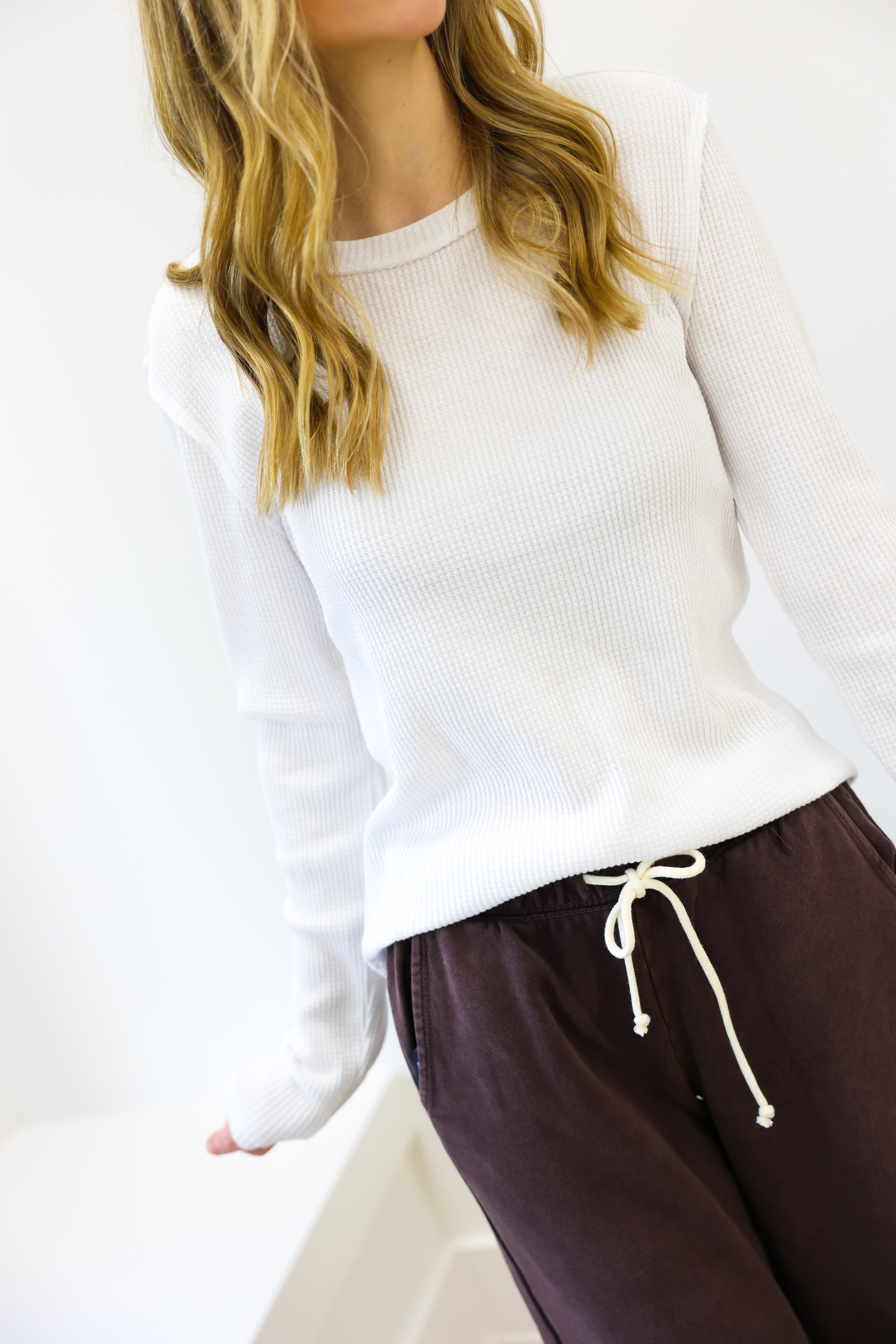 Person wearing a white sweater and brown pants on a plain background