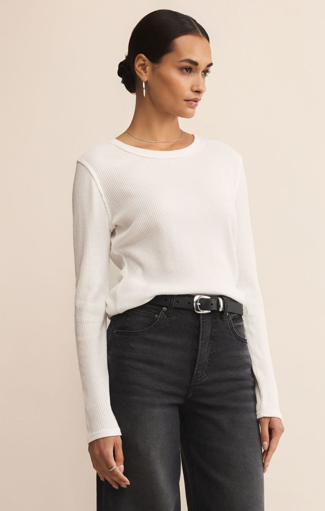 Woman wearing a white long-sleeve top and black jeans against a beige background