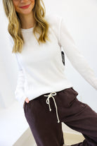 Person wearing a white long-sleeve top and brown pants with a white background
