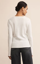 Woman wearing a white sweater and black pants against a beige background
