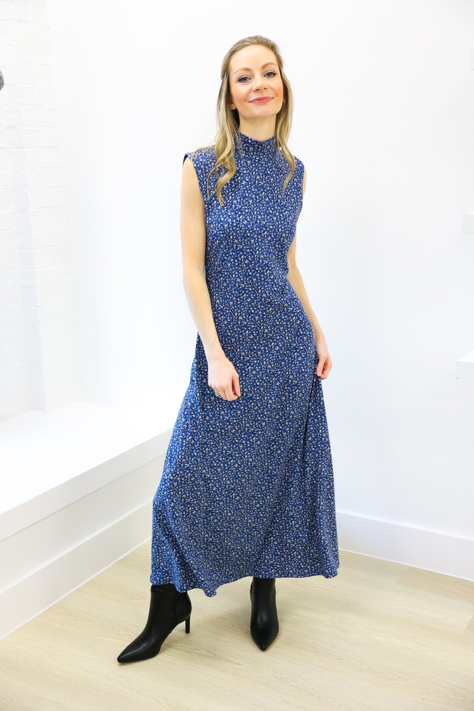 Woman wearing a blue patterned dress standing against a white wall.