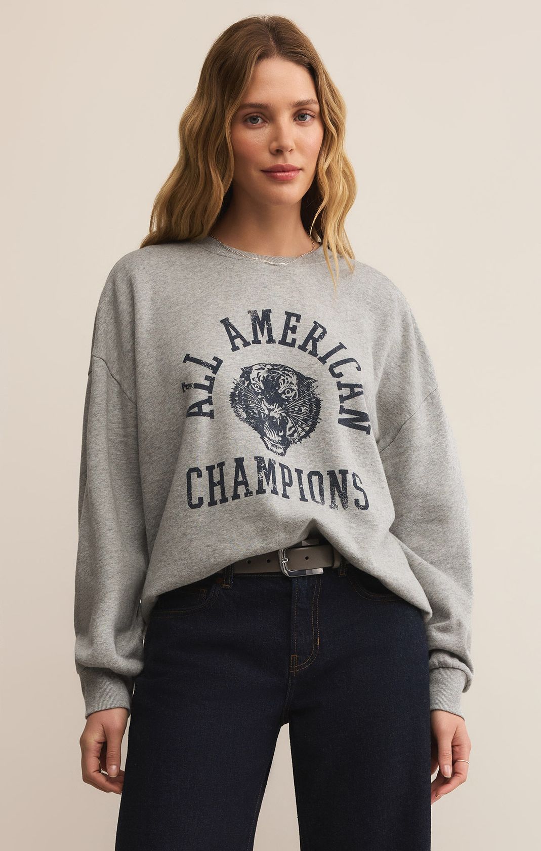 Woman wearing a gray sweatshirt with 'All American Champions' text and graphic, standing against a plain background.