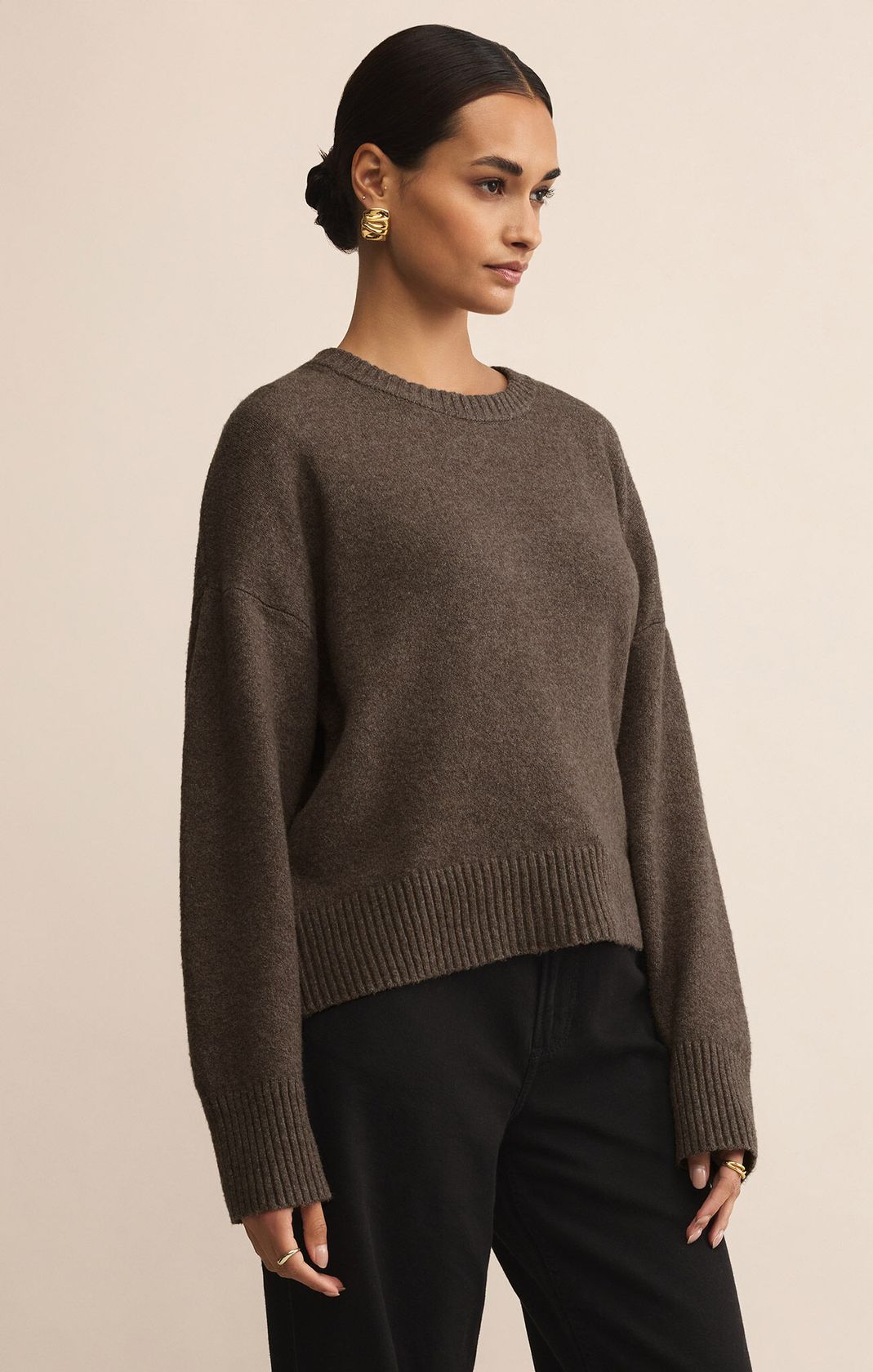 Woman wearing a brown sweater and black pants against a beige background