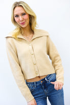 Woman wearing a beige cardigan over a crop top with blue jeans on a white background