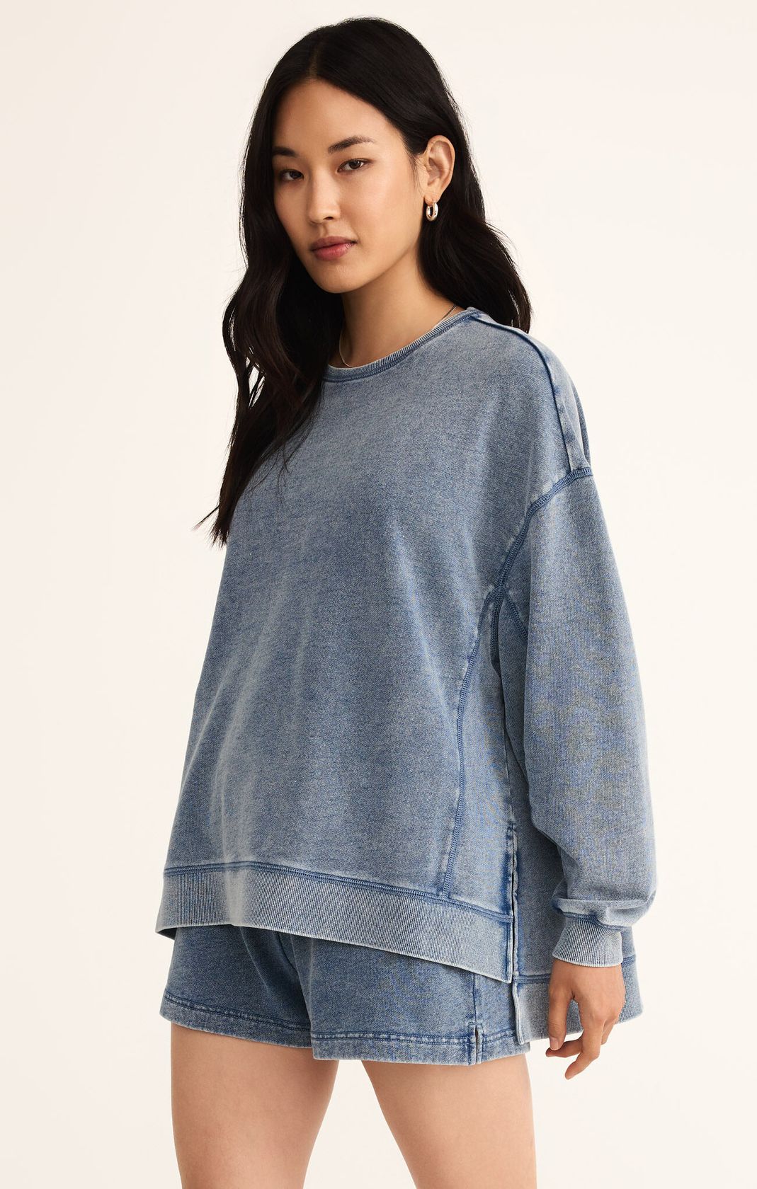 Woman wearing a blue denim sweatshirt and shorts on a beige background