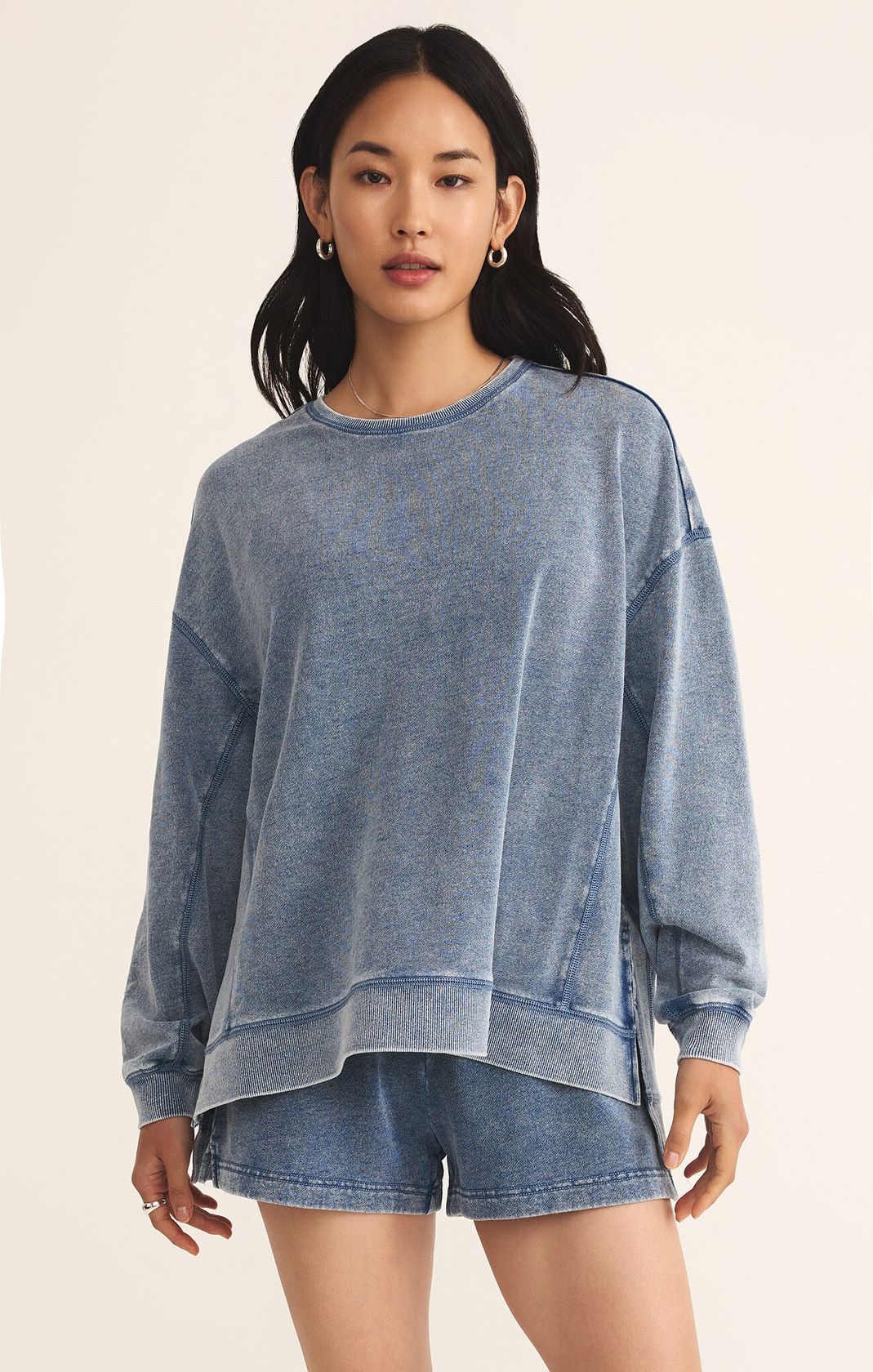 Woman wearing a blue sweatshirt and shorts on a beige background