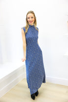 Woman wearing a blue floral dress standing against a white wall.