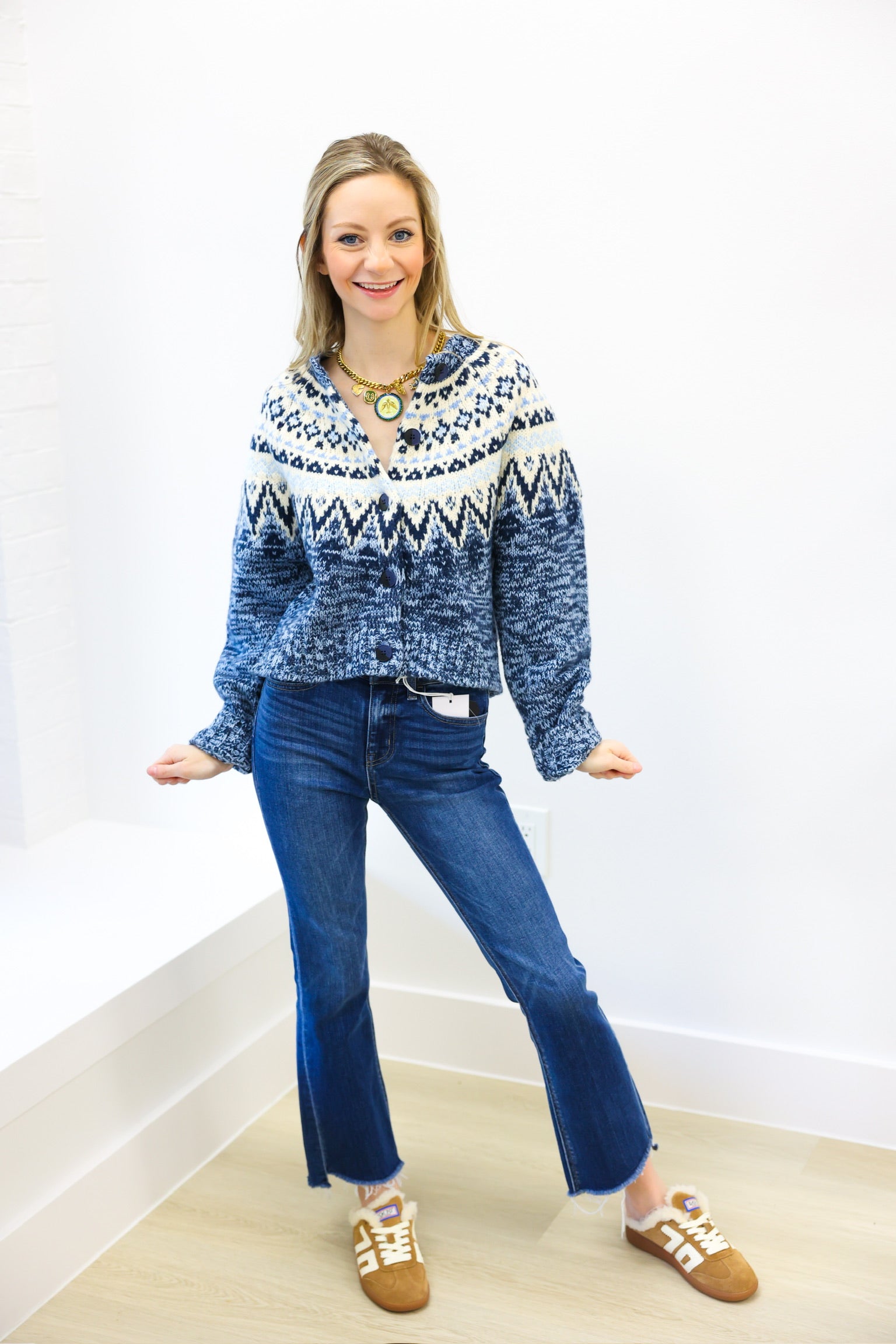 Woman wearing a blue patterned sweater and blue jeans standing against a white wall.