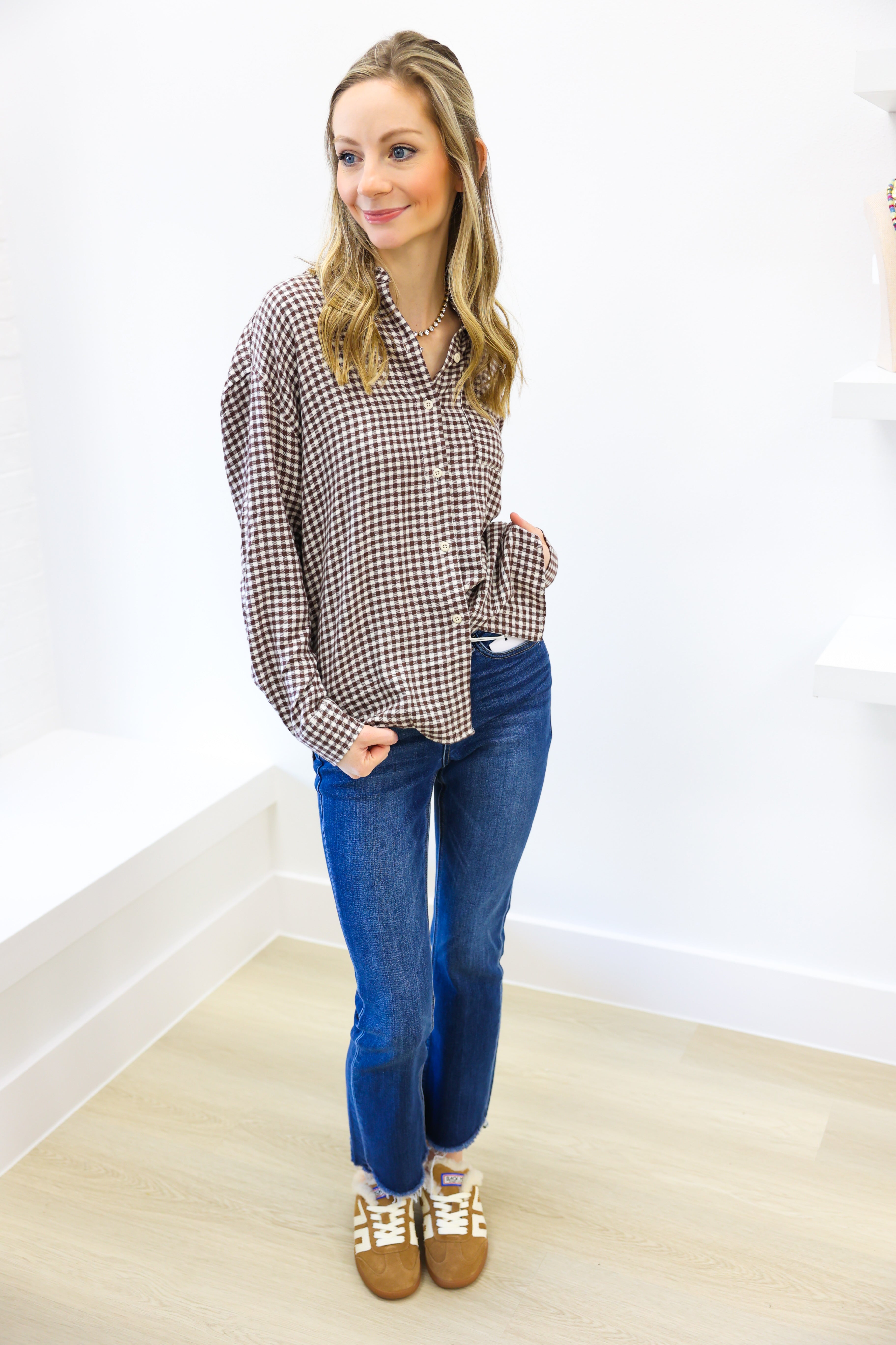Woman wearing a plaid shirt and blue jeans against a white wall.