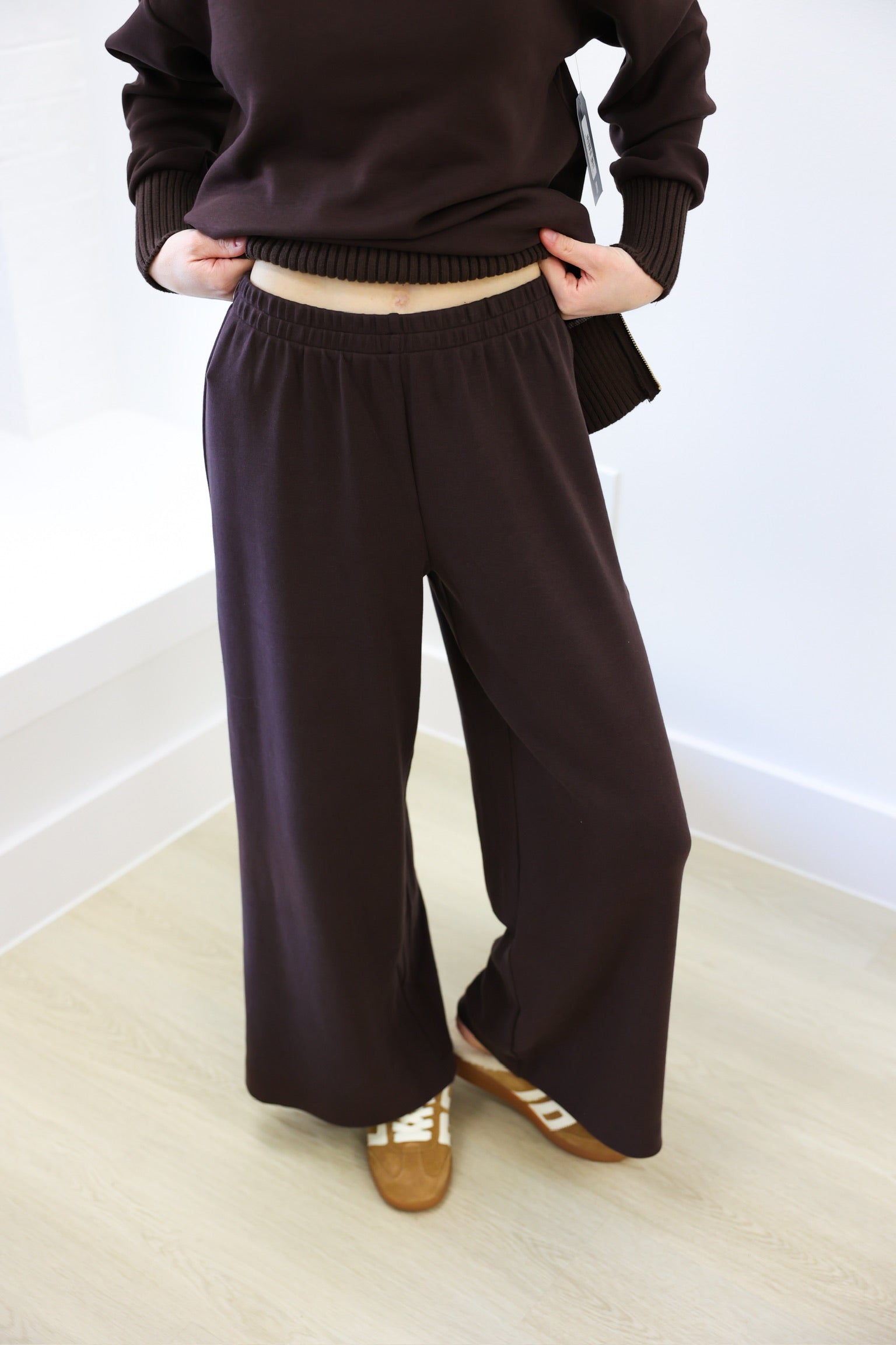 Person wearing a brown sweater and wide-leg pants on a light wooden floor.