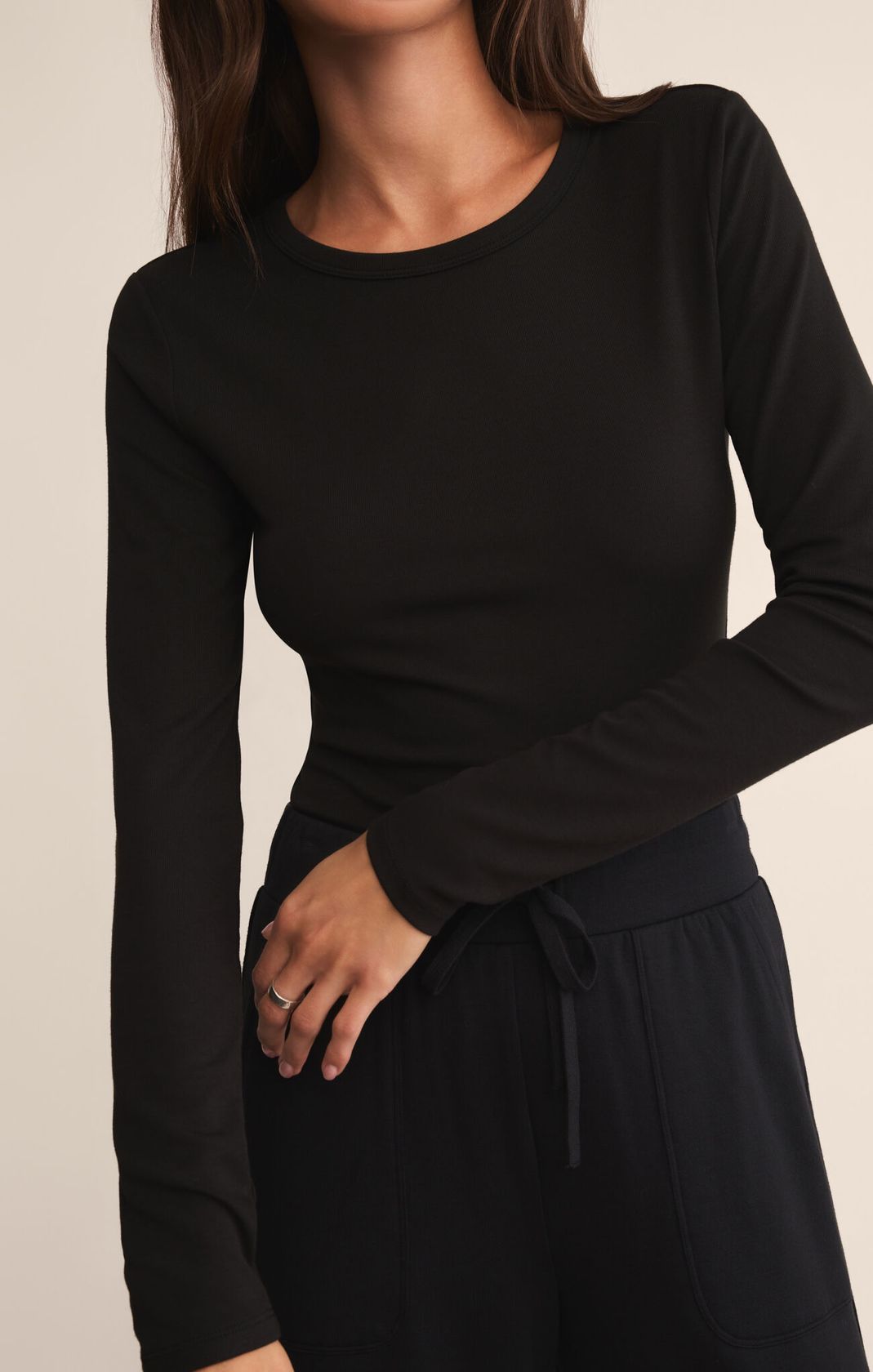 Black long-sleeve top worn by a person on a beige background