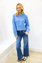 Woman wearing a blue sweater and jeans against a white wall