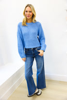 Woman wearing a blue sweater and jeans against a white wall.