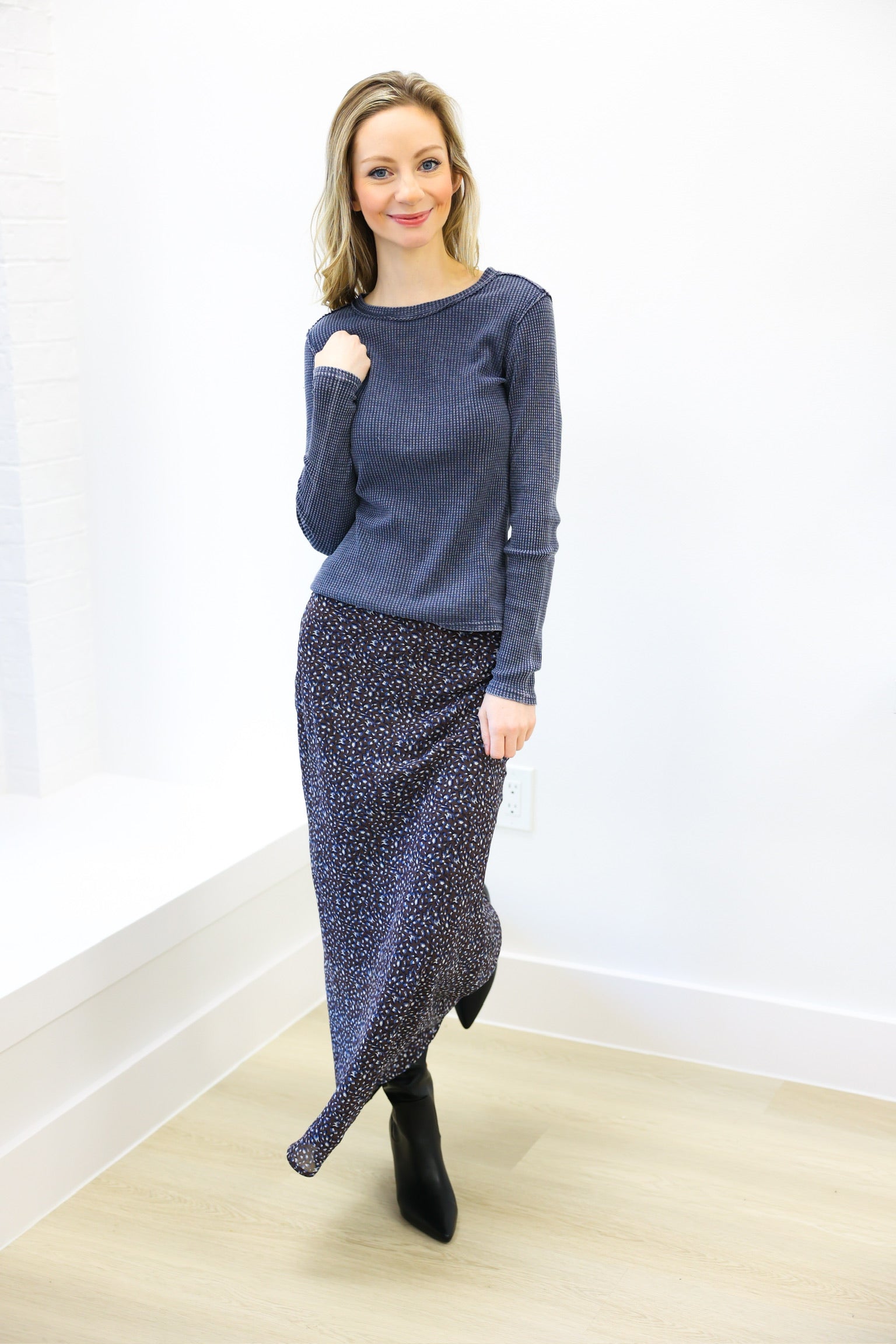 Woman wearing a blue sweater and patterned skirt against a white wall.