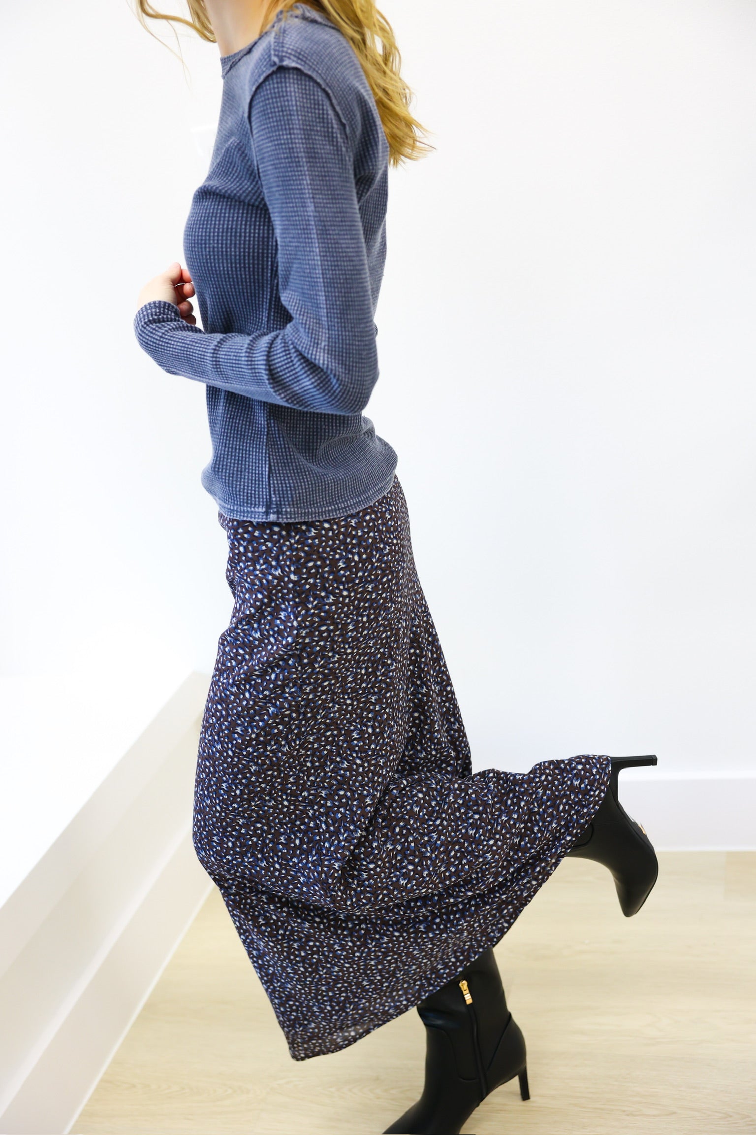 Person wearing a blue sweater and patterned skirt on a white background