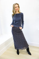 Woman wearing a blue top and patterned skirt against a white wall.