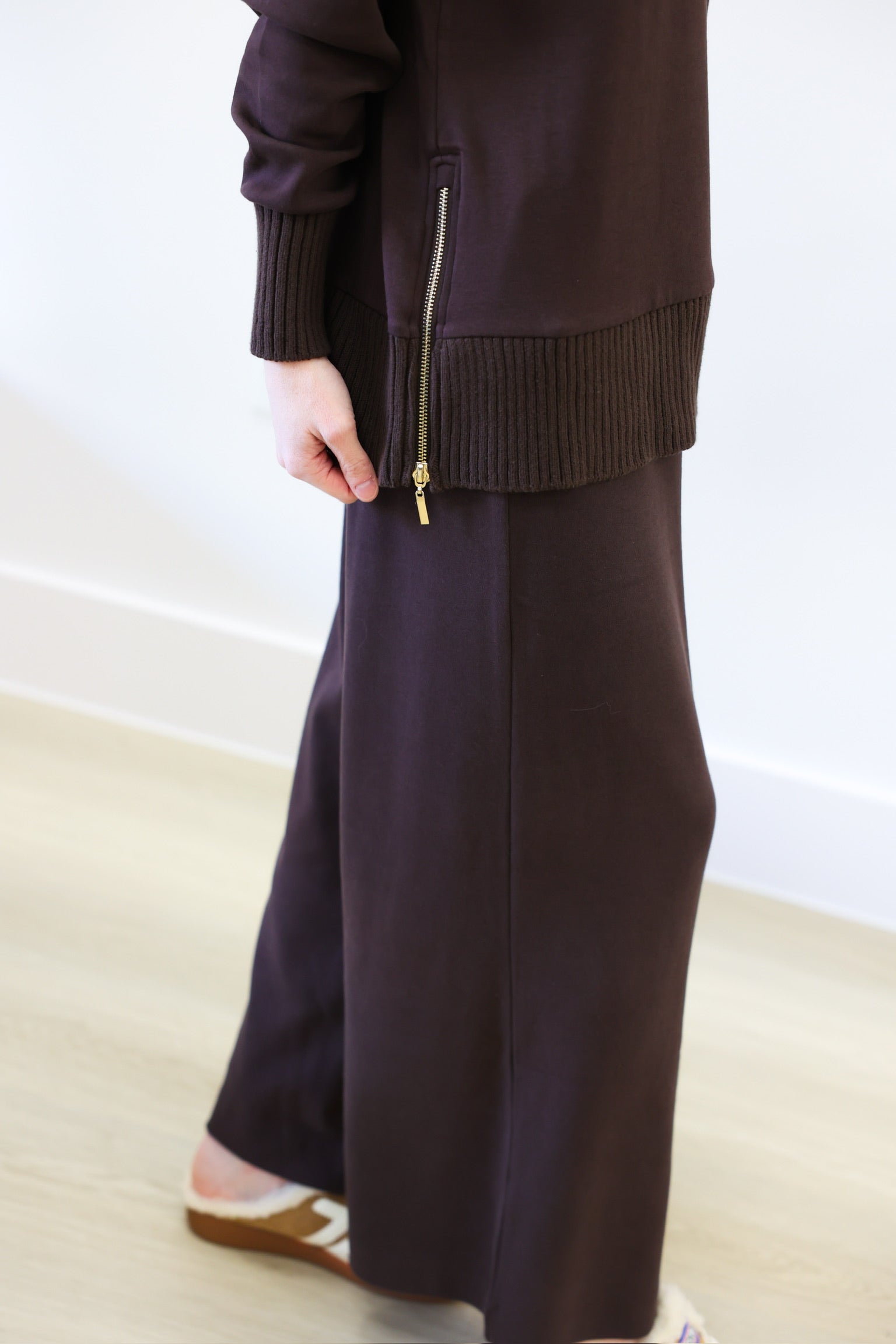 Person wearing a dark brown outfit with wide-leg pants and a jacket.