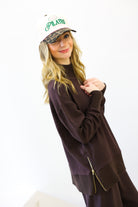 Woman wearing a brown sweater and cap with 'Pilates' text on a white background